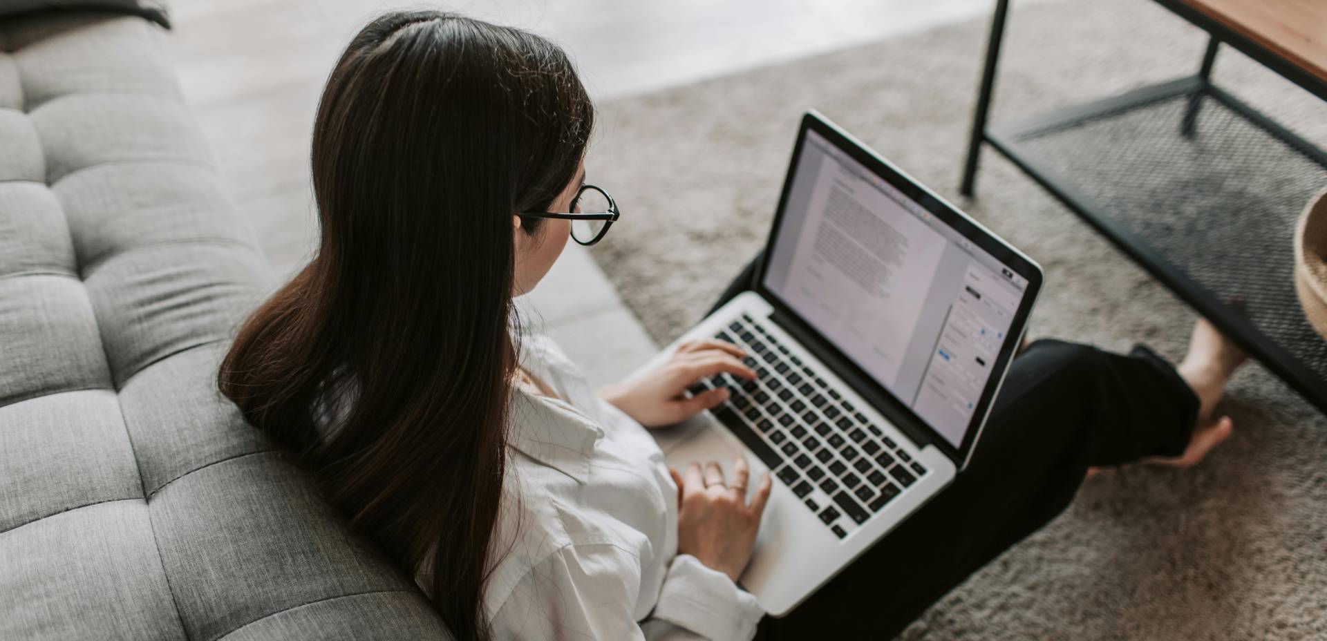 Woman sitting on the floor by her couch using a laptop